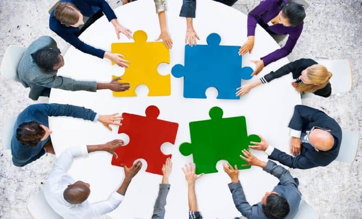 People sitting around a table, each holding one piece of the puzzle