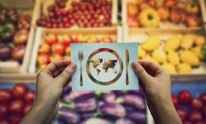 Two hands hold an image of the world in front of boxes of produce